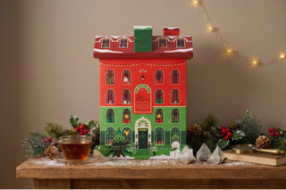 English Tea Shop Sip the Season Christmas Tea House advent calendar displayed on a wooden table beside a fresh cup of tea and festive decorations.