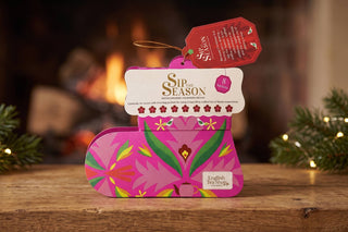 English Tea Shop Sip the Season pink Santa's Stocking holiday organic tea gift box with 8 sachets set on a wooden table in front of a warm fireplace.