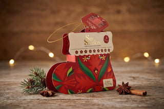 English Tea Shop Sip the Season red Santa's Stocking holiday organic tea gift box with 8 sachets set on a wooden table with festive lights.