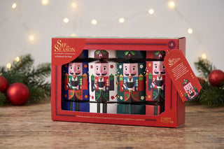 English Tea Shop Sip the Season nutcracker collection displayed on a rustic wooden table with Christmas ornaments and pine branches in the background.